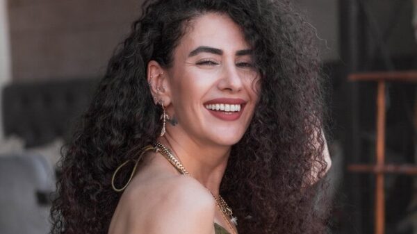Smiling woman with curly hair wearing an olive green dress.