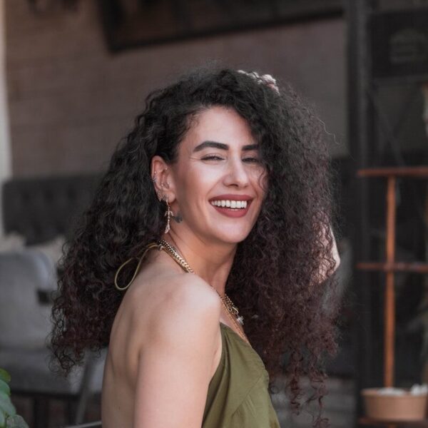 Smiling woman with curly hair wearing an olive green dress.