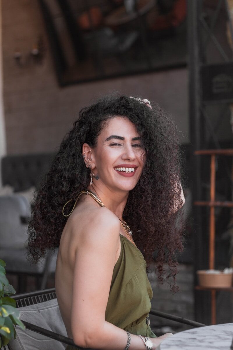 Smiling woman with curly hair wearing an olive green dress.