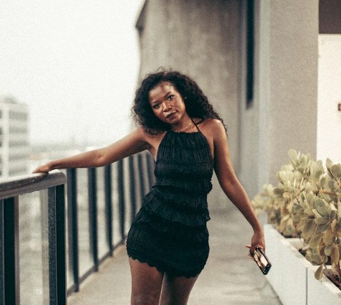 Woman poses on a balcony overlooking a cityscape.