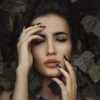 Woman with eyes closed surrounded by dark leaves