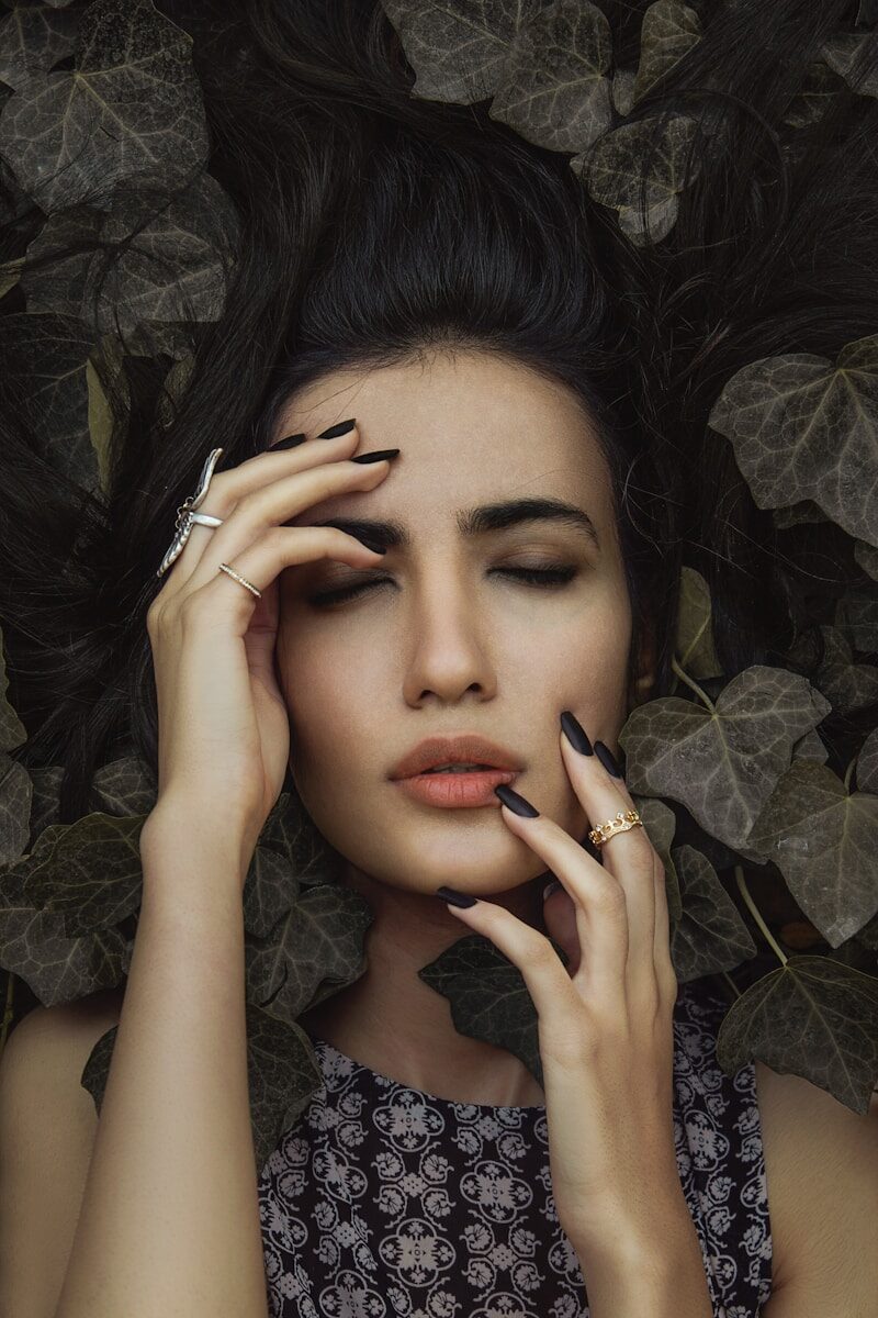 Woman with eyes closed surrounded by dark leaves