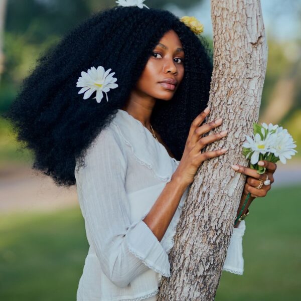 Woman with flowers in hair embraces tree, exuding natural beauty and elegance.