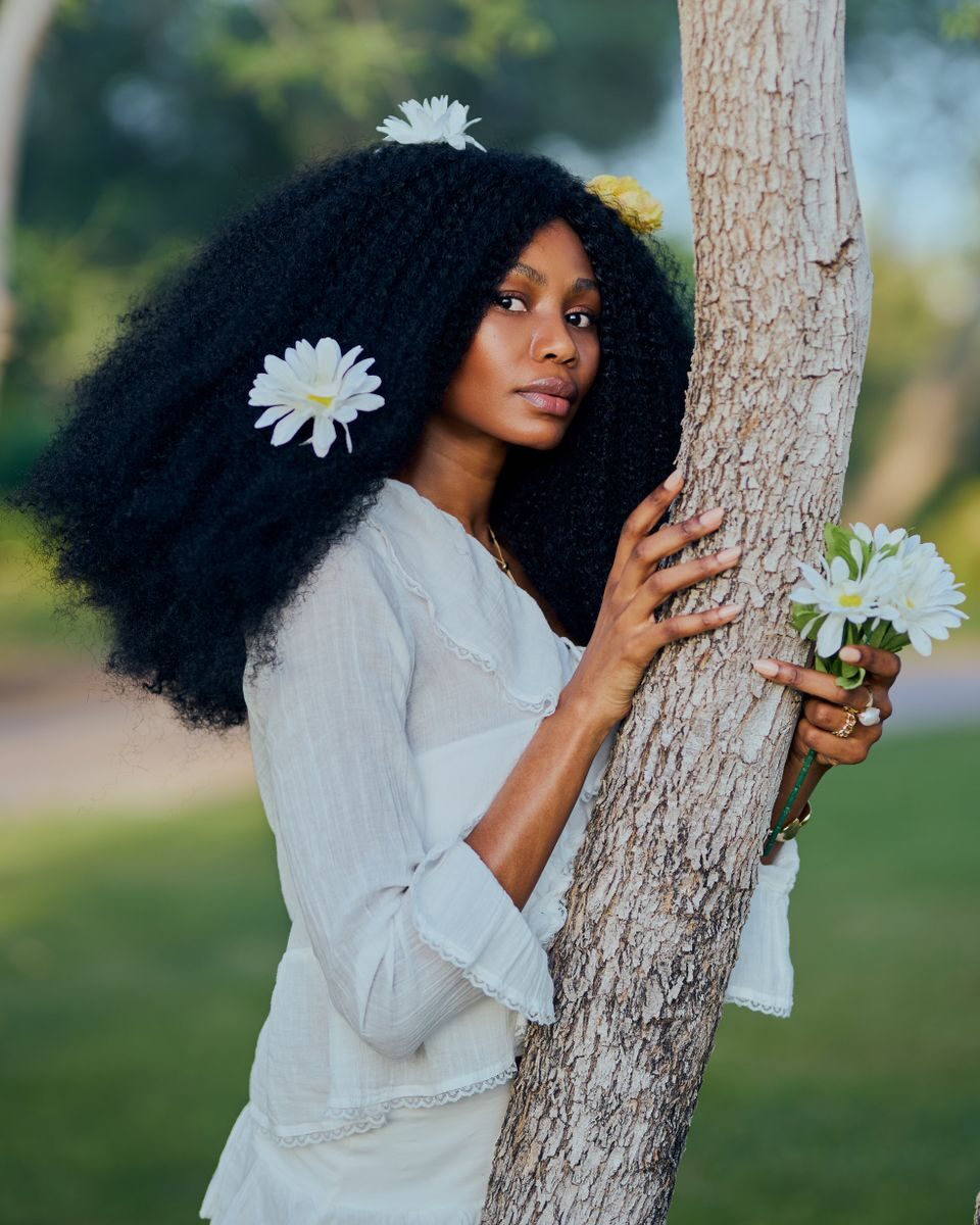 Woman with flowers in hair embraces tree, exuding natural beauty and elegance.