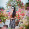 Smiling woman in floral skirt enjoys a sunny day surrounded by colorful flowers outdoors.