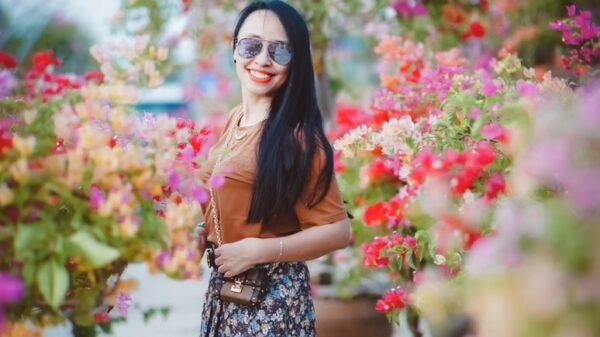 Smiling woman in floral skirt enjoys a sunny day surrounded by colorful flowers outdoors.