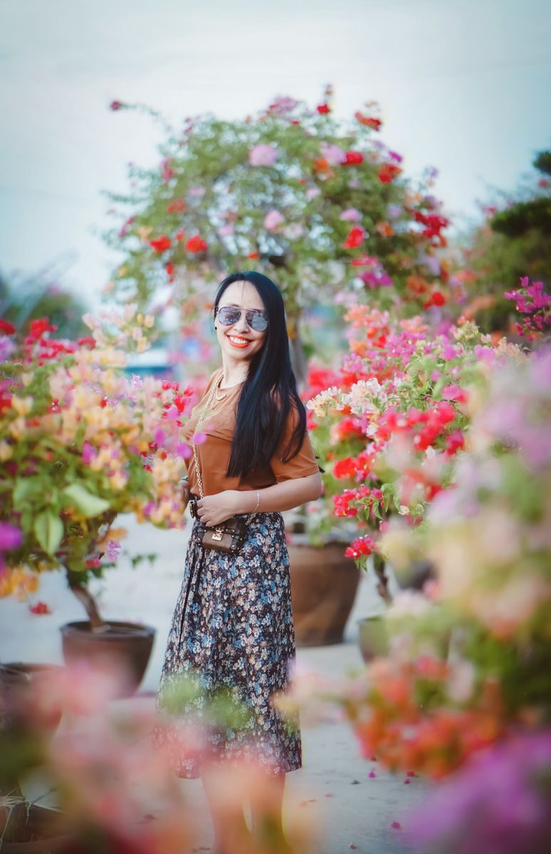 Smiling woman in floral skirt enjoys a sunny day surrounded by colorful flowers outdoors.